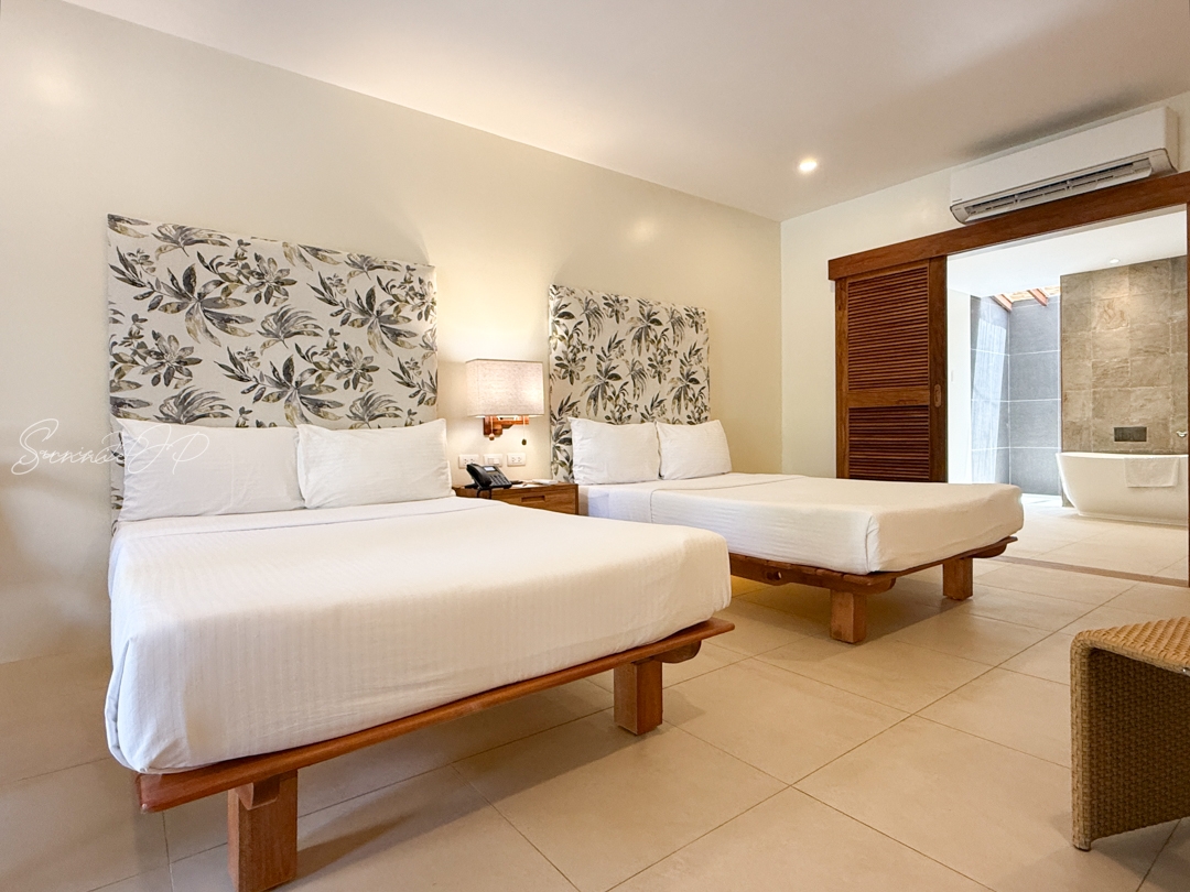 ブルーウォーターマリバゴのアムマスパスイート客室。広々としたツインベッドで心地よい眠りを楽しめる空間。